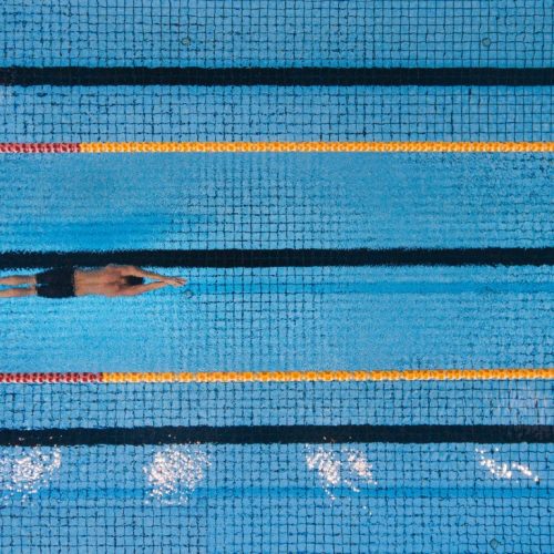 Top view shot of young man swimming laps in a swimming pool. Male swimmer gliding through the water.